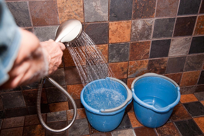 Pexels photo of a person collecting shower water in a bucket, sunlight streaming into a bathroom, eco-friendly aesthetic