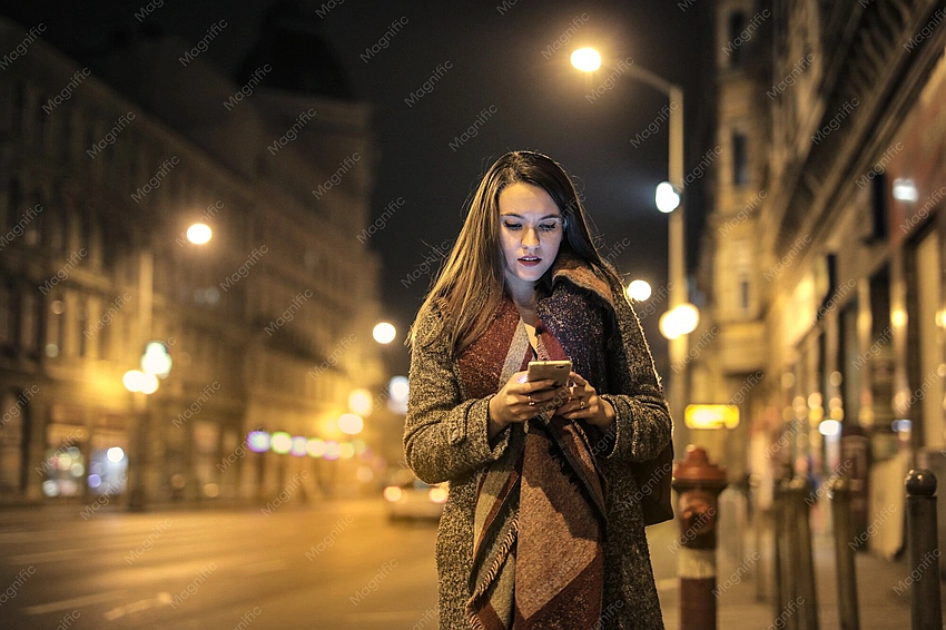 Teen girl texting on phone, city street at night