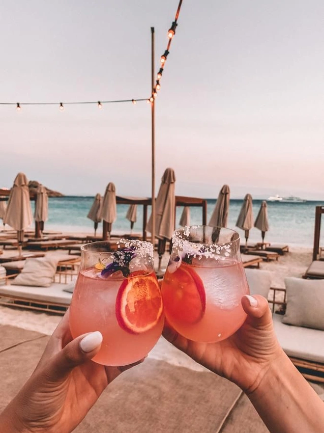 Glamorous women sipping cocktails on a beach in Mykonos