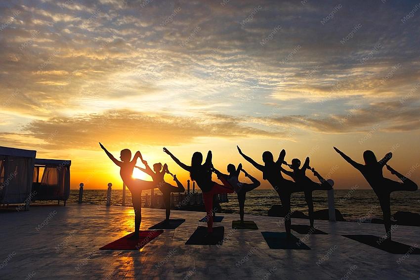 Women doing yoga on a beach at sunrise, boho style
