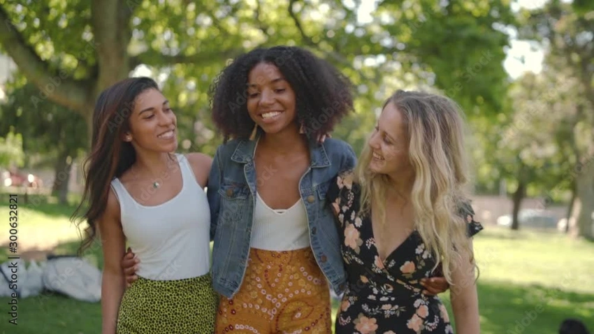 Diverse group of happy, smiling young women walking arm-in-arm in a park