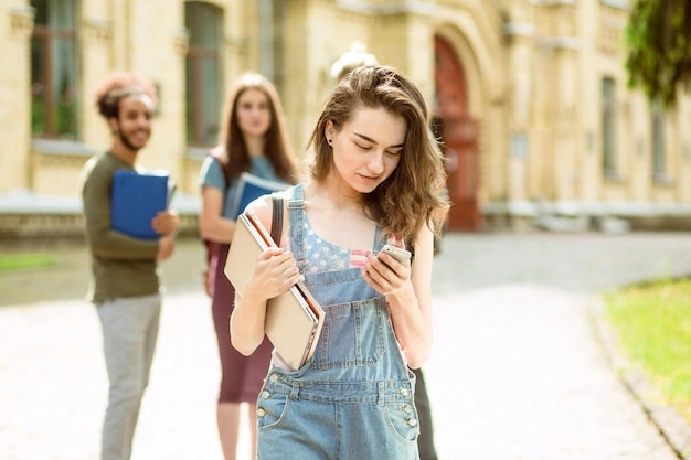 Young woman looking thoughtfully at phone, group of friends in background, slightly blurred