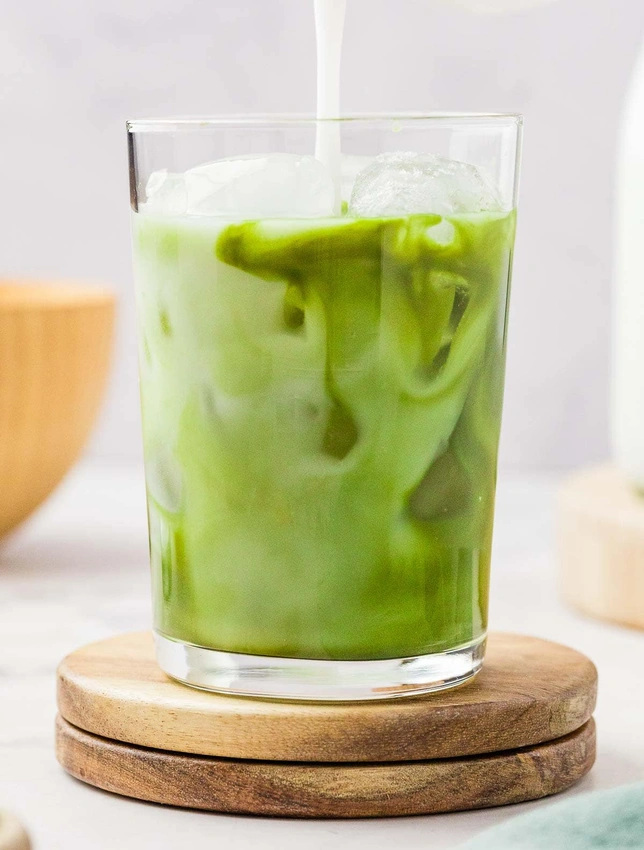 Frothed oat milk in glass, iced matcha latte pouring milk